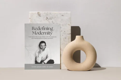 Book titled 'Redefining Modernity' placed on a desk with a donut-shaped sculpture positioned on top, creating a contemporary and stylish display.